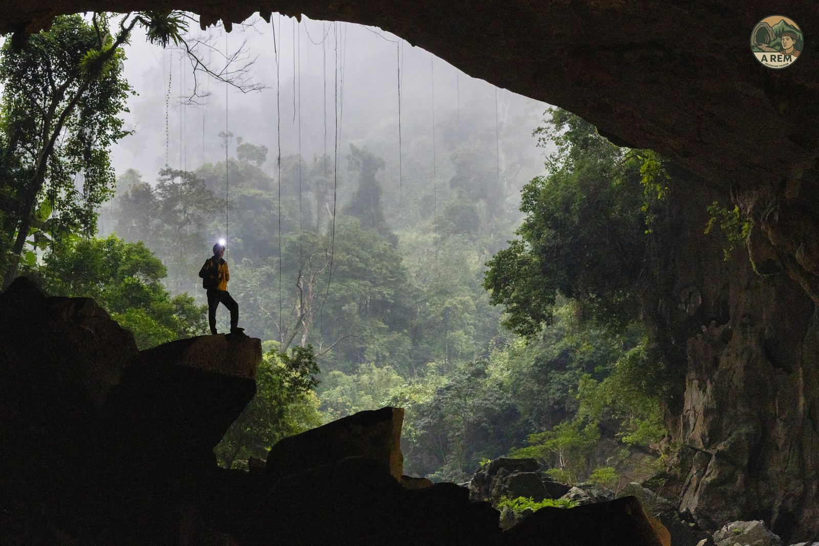 Misty view of a Phong Nha cave entrance from inside, silhouette of a caver at the edge