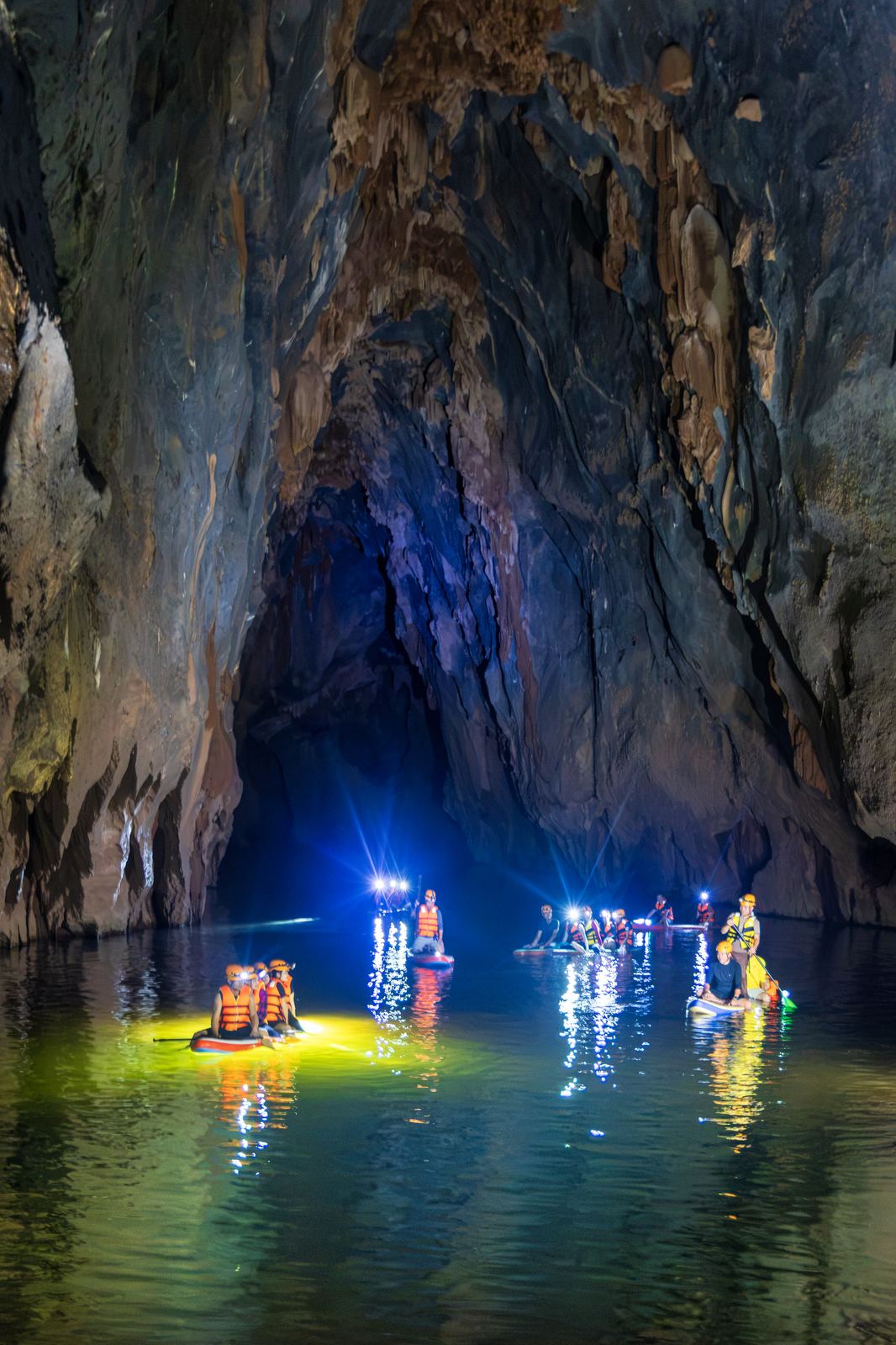Group SUP paddling through Kling Cave with glowing lights reflected in the water
