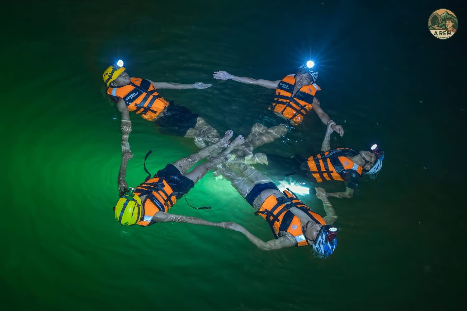 Group of swimmers with headlamps forming a star pattern in glowing green underground water