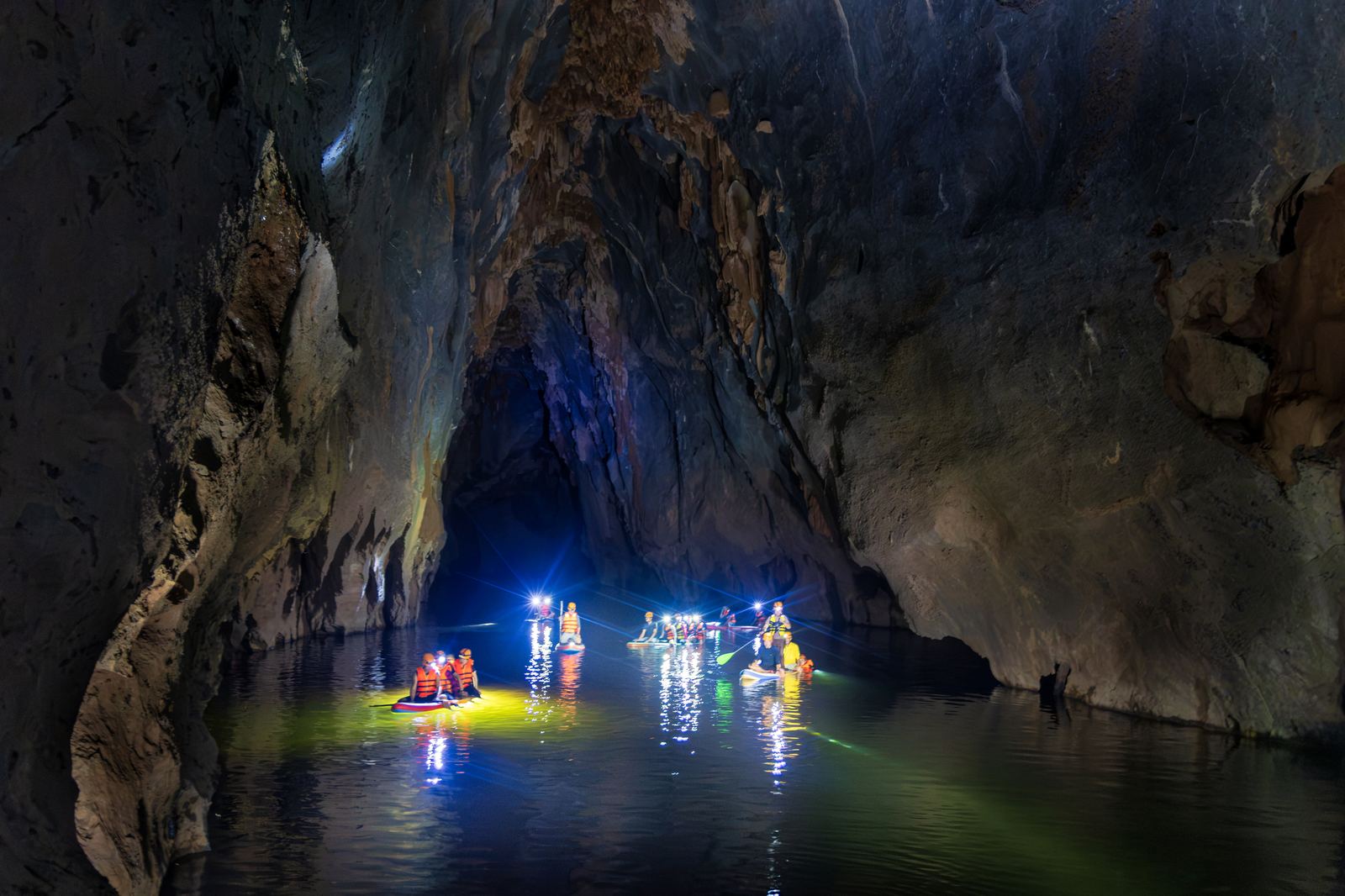 Group kayaking through Kling Cave lit by colorful headlamps