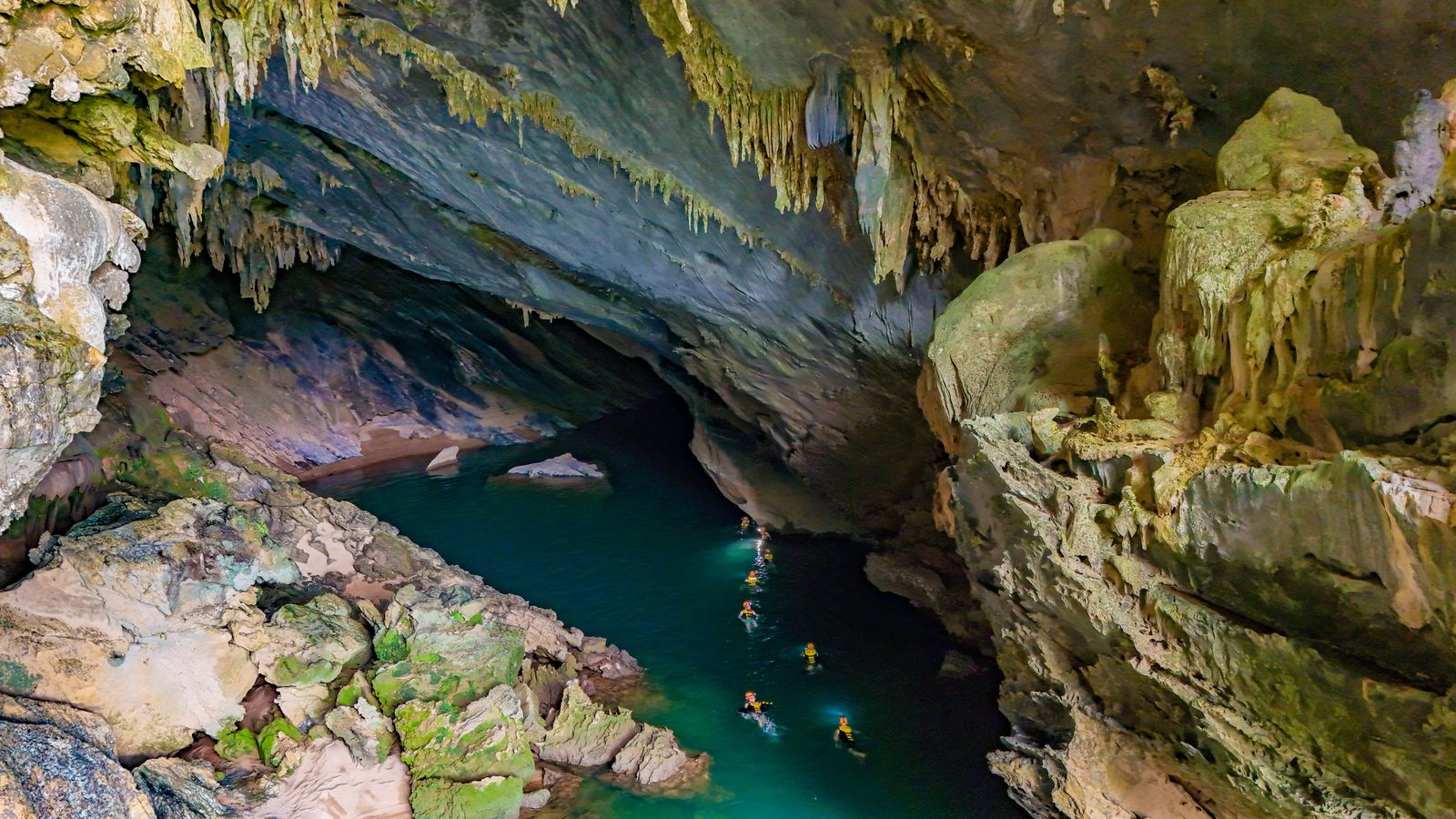 Aerial view of the turquoise pool inside Hang Tra Ang cave, surrounded by jungle